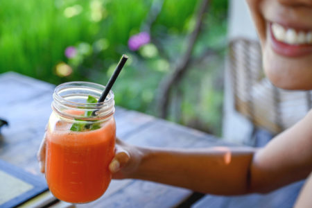 Mulher sorridente segurando suco de cenoura espremido na hora. Suco para emagrecimento.