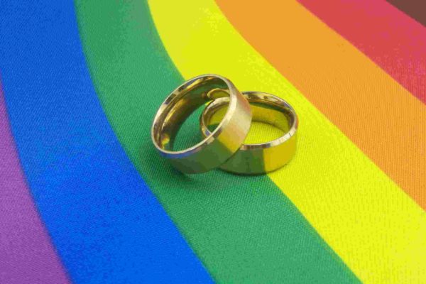 Na foto, alianças de casamento sobre bandeira LGBT+