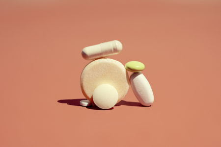 Foto mostra pílulas e suplementos empilhados em fundo cor terroso
