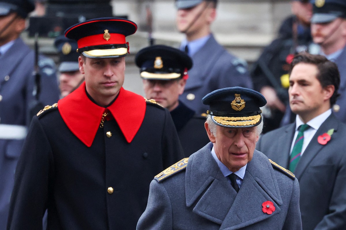 Charles e William estão usando trajes militares. William é um homem calvo, de 41 anos, usa um traje preto com detalhes vermelhos. Charles é um homem velho, calvo e está usando um traje cinza - Metrópoes