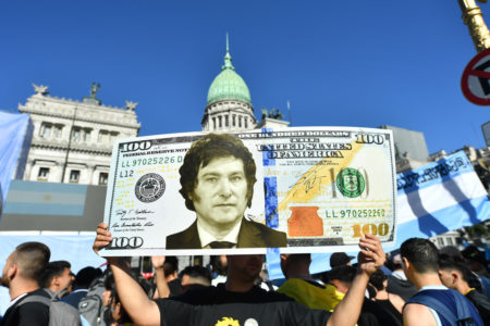 Apoiador de Javier Milei segura uma nota de dólar gigante com o rosto do presidente eleito, enquanto as pessoas começam a se reunir do lado de fora do Congresso Nacional Argentina