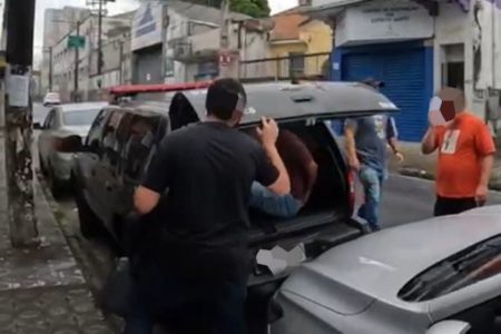 Em foto colorida homem é colocado em porta-malas de viatura policial - Metrópoles