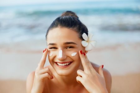 mulher com uma flor no cabelo passando protetor solar