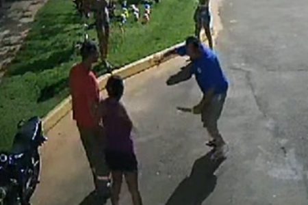 Em foto colorida homem com sobrepeso e camiseta azul segura faca, apontando-a contra duas pessoas; ele esfaqueou o síndico do condomínio onde mora após ser multado por não recolher cocô de cachorro - Metrópoles