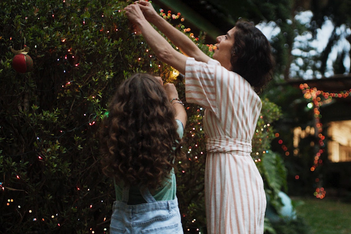 Foto colorida de uma criança ao lado de uma mulher enfeitando uma árvore de Natal - Metrópoles