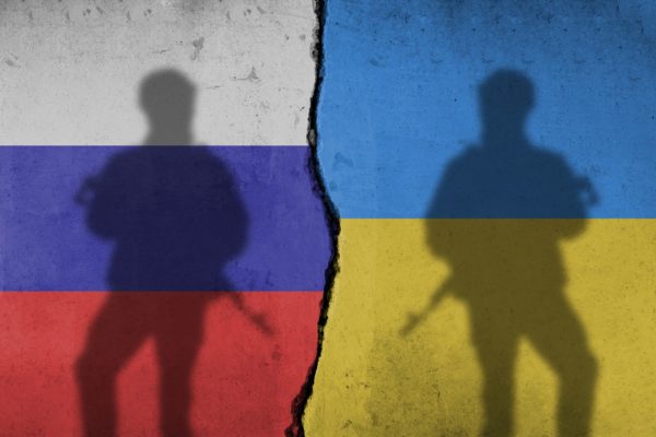 Imagem colorida de sombras de dois soldados em frente de parede pintada nas cores das bandeiras de Rússia (esquerda) e Ucrânia (direita) - Metrópoles