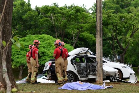 Carro branco destruído após acidente, ambulância e bombeiros do lado