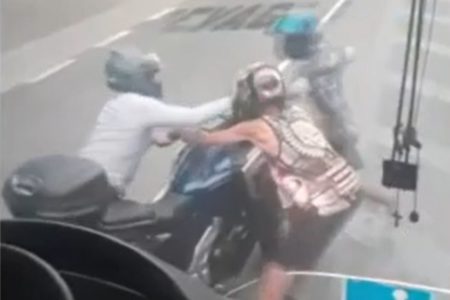 Imagem de dois assaltantes de capacete tentando pegar moto de motociclista em avenida - Metrópoles