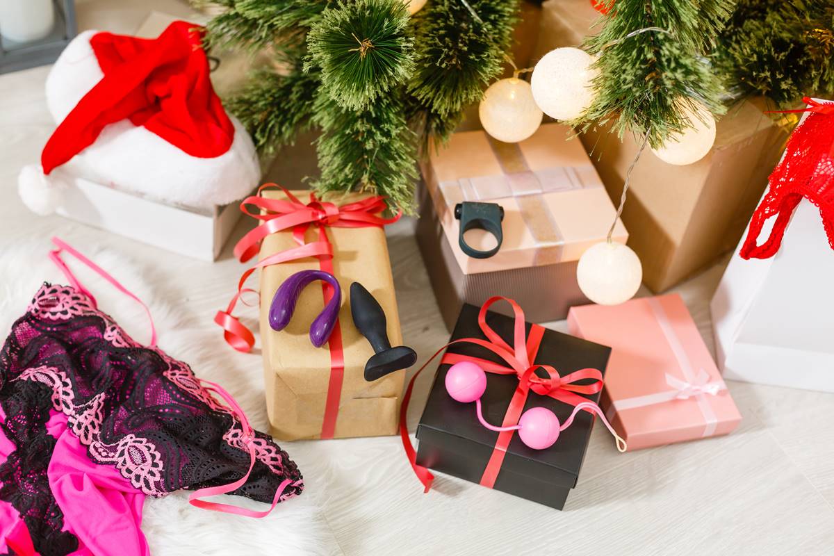 Foto colorida de vários sex toys em cima de caixas de presentes embaixo de uma árvore de natal com um gorro de papai noel - Metrópoles