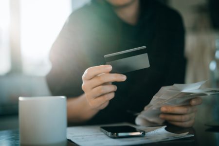 Imagem de pessoa segurando o cartão de crédito com uma mão e as contas com outra - Metrópoles