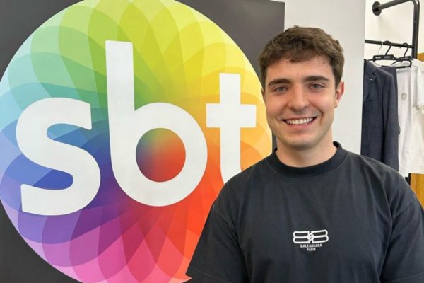 Foto colorida de João Augusto Liberato, filho de Gugu ao lado da logo do SBT - Metrópoles