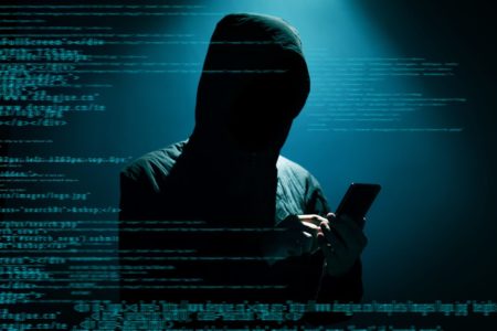 Imagem de pessoa digitando em aparelho celular. O homem usa um capuz e seu rosto não aparece. O fundo da imagem é escuro e sombrio - Metrópoles