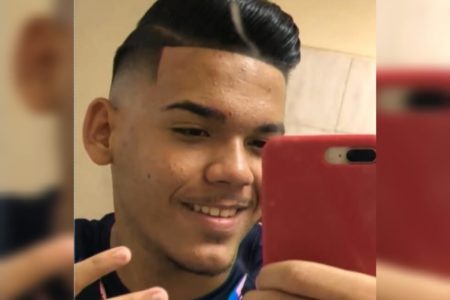 Imagem de jovem negro sorrindo com celular vermelho na mão - Metrópoles