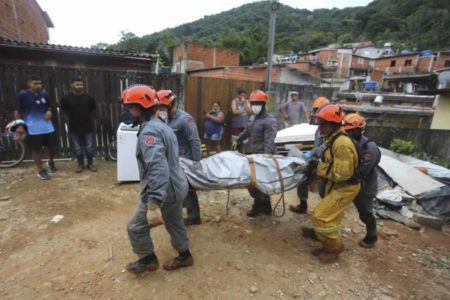 Quatro bombeiros carregam corpo coberto com lona em meio à lama - Metrópoles