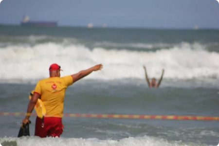 Imagem colorida de guarda vidas sinalizando para pessoa se afogando em mar - Metrópoles