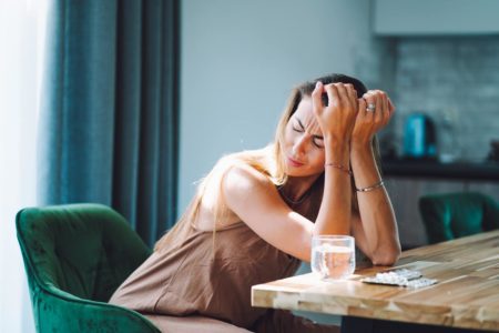 Mulher com mais na cabeça em frente à mesa com copo e remédios - Metrópoles