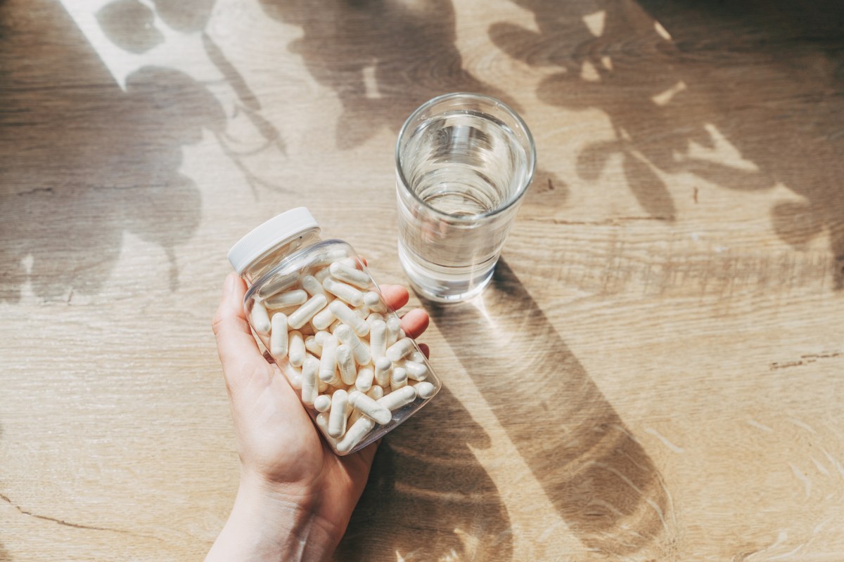 Pote com cápsulas de vitamina D ao lado de um copo embaixo da luz solar