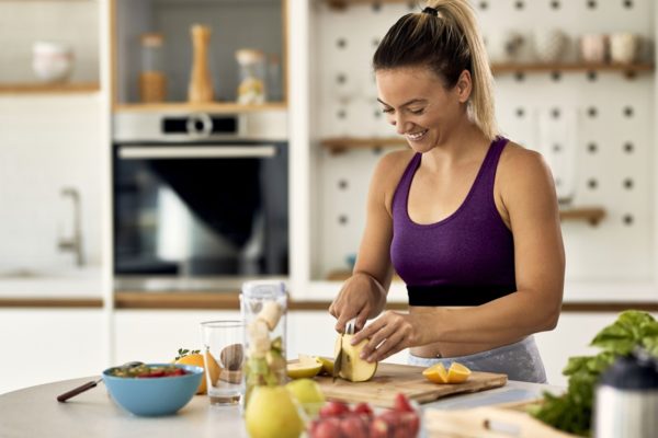 Foto colorida de mulher cortando frutas em uma cozinha - Metrópoles