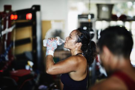 Foto colorida de uma mulher suada bebendo água durante o exercício físico - Metrópoles