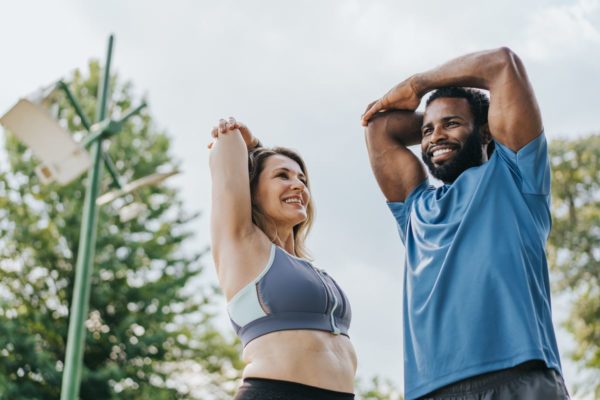 Mulher branca e homem alto, negro estão se alongando para fazer exercícios físicos - Metrópoles