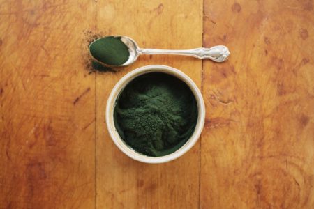Foto mostra uma xícara e uma colher com uma porção de spirulina, que é um pó esverdeado - Metrópoles