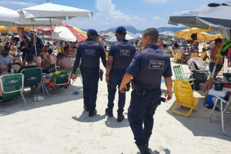 Imagem colorida mostra fiscais da Prefeitura do Guarujá, no litoral de São Paulo, andando pela praia para fiscalizar o uso de caixas de som - Metrópoles