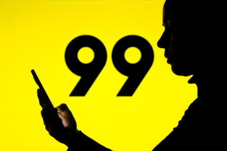 Imagem de homem mexendo no celular. Ao fundo, o logotipo da 99 - Metrópoles