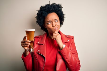 Foto colorida de mulher com blusa e jaqueta vermelha. Ela está segurando um copo de chopp - Metrópoles