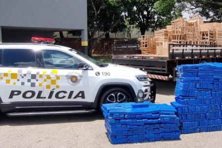 Imagem colorida mostra 991 tijolos de maconha apreendidos com caminhoneiro ao lado de um carro de polícia - Metrópoles