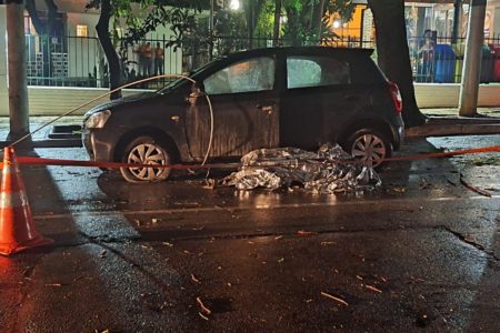 Imagem colorida mostra corpo coberto ao lado de carro preto; vítima foi eletrocutada após fio de alta tensão enroscar no espelho retrovisor do veículo - Metrópoles