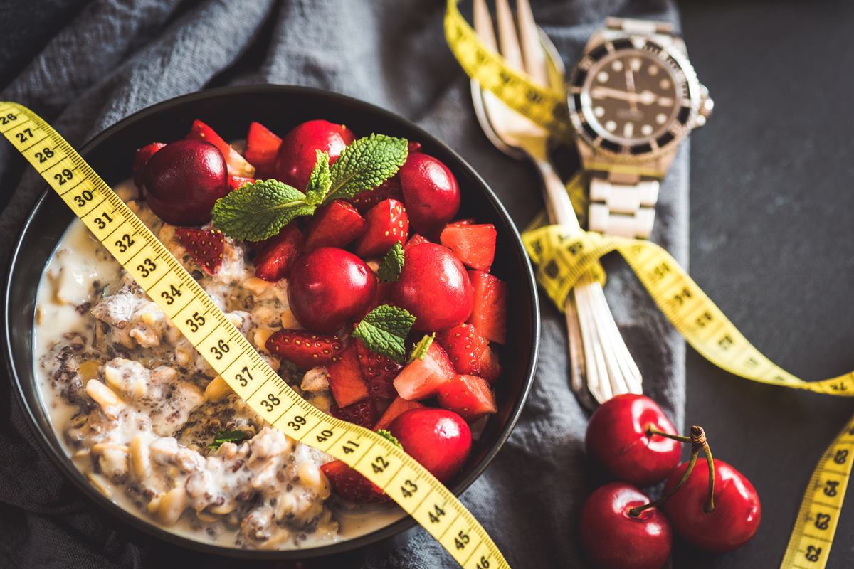 Foto colorida de bowl com frutas cortadas. Em cima, tem uma fita métrica amarela. Ao lado, tem um garfo e um relógio - Metrópoles