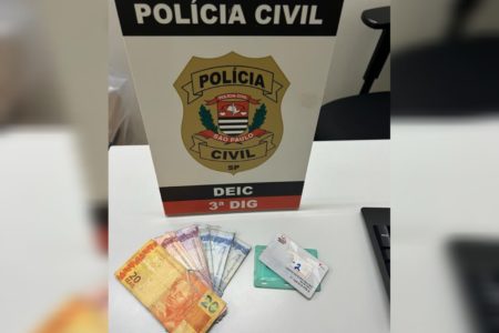 Imagem de placa da Polícia Civil com cédulas de reais e bilhete de transporte - Metrópoles