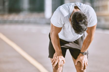 Homem com as mãos nos joelhos e cabeça abaixada após exercício físico - Metrópoles