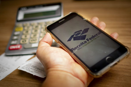 Imagem colorida de um celular com o símbolo da Receita Federal Imposto de Renda consulta - Metrópoles