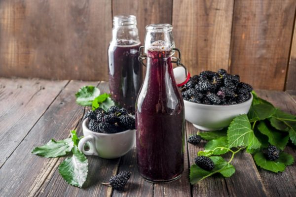 Duas garrafas com suco de amora e potes da fruta ao redor