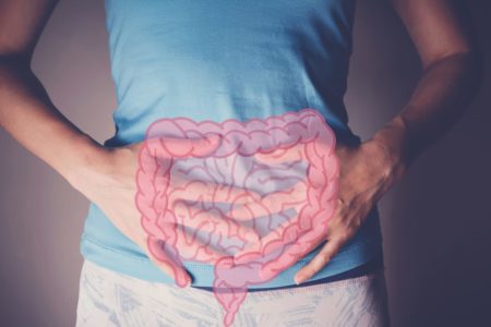 Mulher com as mãos no intestino e um desenho do órgão em cima. A mulher usa blusa azul e a foto mostra apenas o seu tronco - Metrópoles - câncer de intestino