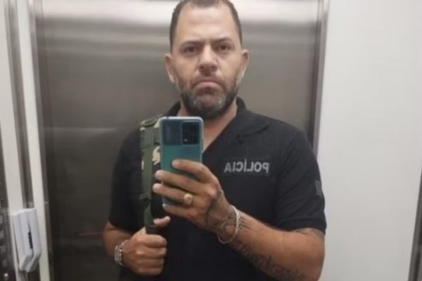 Imagem de homem com uniforme de policial penal com celular na mão - Metrópoles