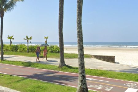 Foto mostra jardim da praia no bairro Jardim Real, em Praia Grande, com dois turistas andando na calçada - Metrópoles