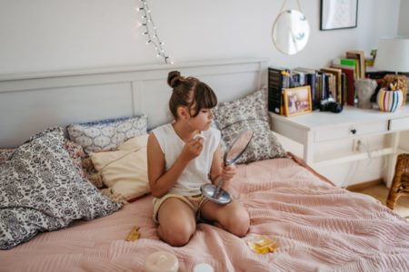 Menina se olha no espelho sentada em cama - Metrópoles