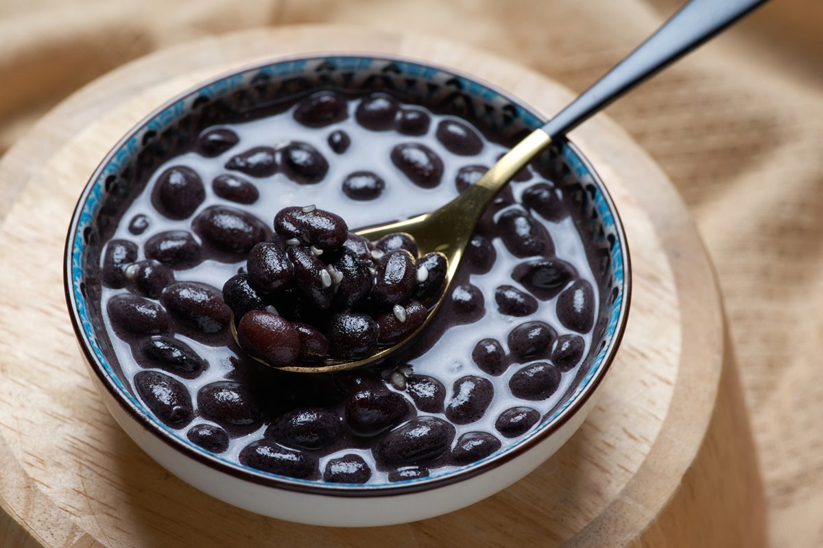Foto de feijão preto dentro de uma tigela. Há uma colher com o alimento - Metrópoles