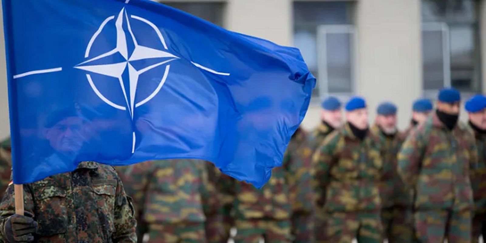 Imagem de vários soldados enfileirados, com um soldado a frente, segurando a bandeira da Otan - Metrópoles