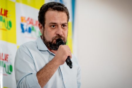 economista Imagem colorida mostra Guilherme Boulos falando ao microfone. Ele é um homem branco, de cabelo e barba castanhos, e veste camisa branca