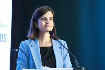 Imagem colorida mostra Tabata Amaral, mulher branca, de cabelos pretos, de terno azul e blusa preta, em imagem do peito para cima, na frente de um microfone - Metrópoles