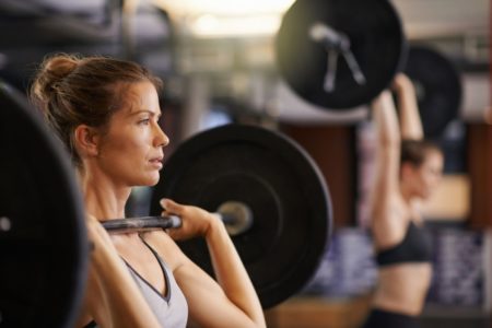 Foto colorida de mulher sustentando uma barra na academia