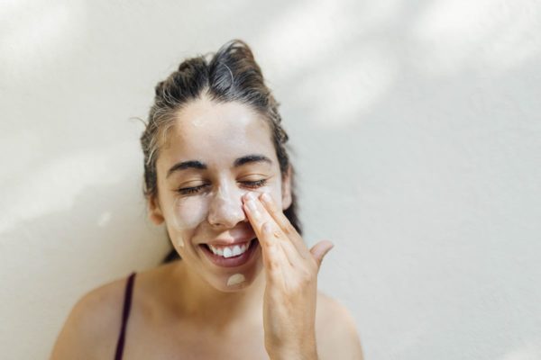 Mulher, cabelo preto, com a mão no rosto espalhando o protetor solar