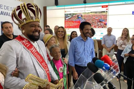 Imagem colorida mostra Ricardo Nunes, de camisa azul, com o rei momo do Carnaval e outras pessoas - Metrópoles