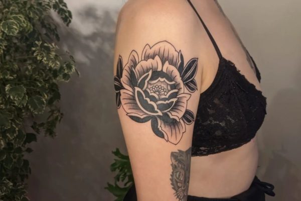 Mulher branca de lado com uma flor tatuada no braço