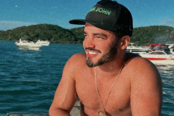 Foto colorida de Fábio Gontijo usando boné, sem camisa, com fundo na praia - Metrópoles