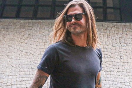 Dado Dolabella é clicado, sorridente, de blusa preta, óculos escuros e cabelos soltos - Metrópoles