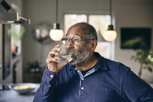 Imagem mostra idoso negro de camisa social azul, bebendo um copo de água - Metrópoles